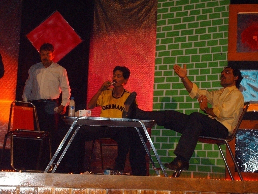Photo d'archive d'Afghanistan. Compagnie Hasards d'Hasards. Photo de représentation de spectacle de la compagnie de la radio et télévision Afghane. Trois comédiens sur scène autour d'une table.