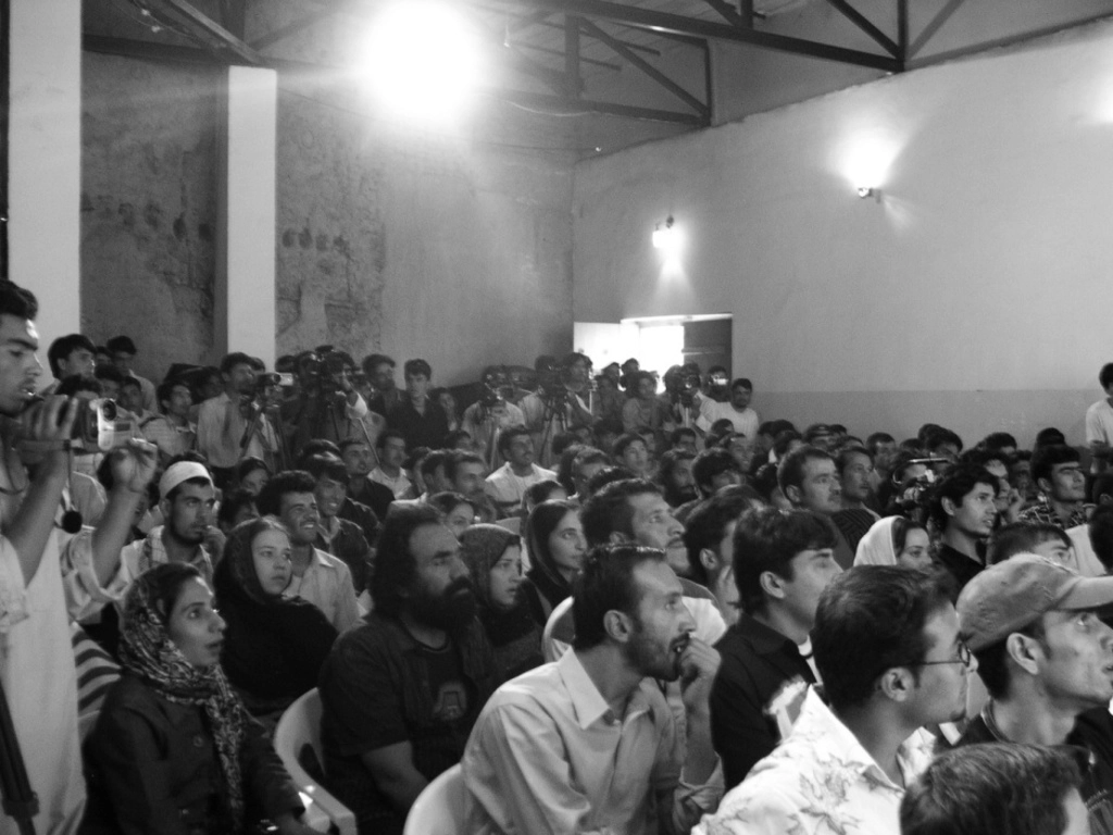 Photo d'archive d'Afghanistan. Compagnie Hasards d'Hasards. Photo en noir et blanc du public. Des visages attentifs. Des hommes film le spectacle.