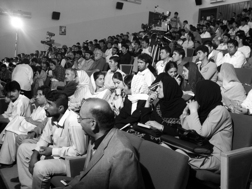Photo d'archive d'Afghanistan. Compagnie Hasards d'Hasards. Photo en noir et blanc du public. Des gens discutent. Des hommes film le spectacle.